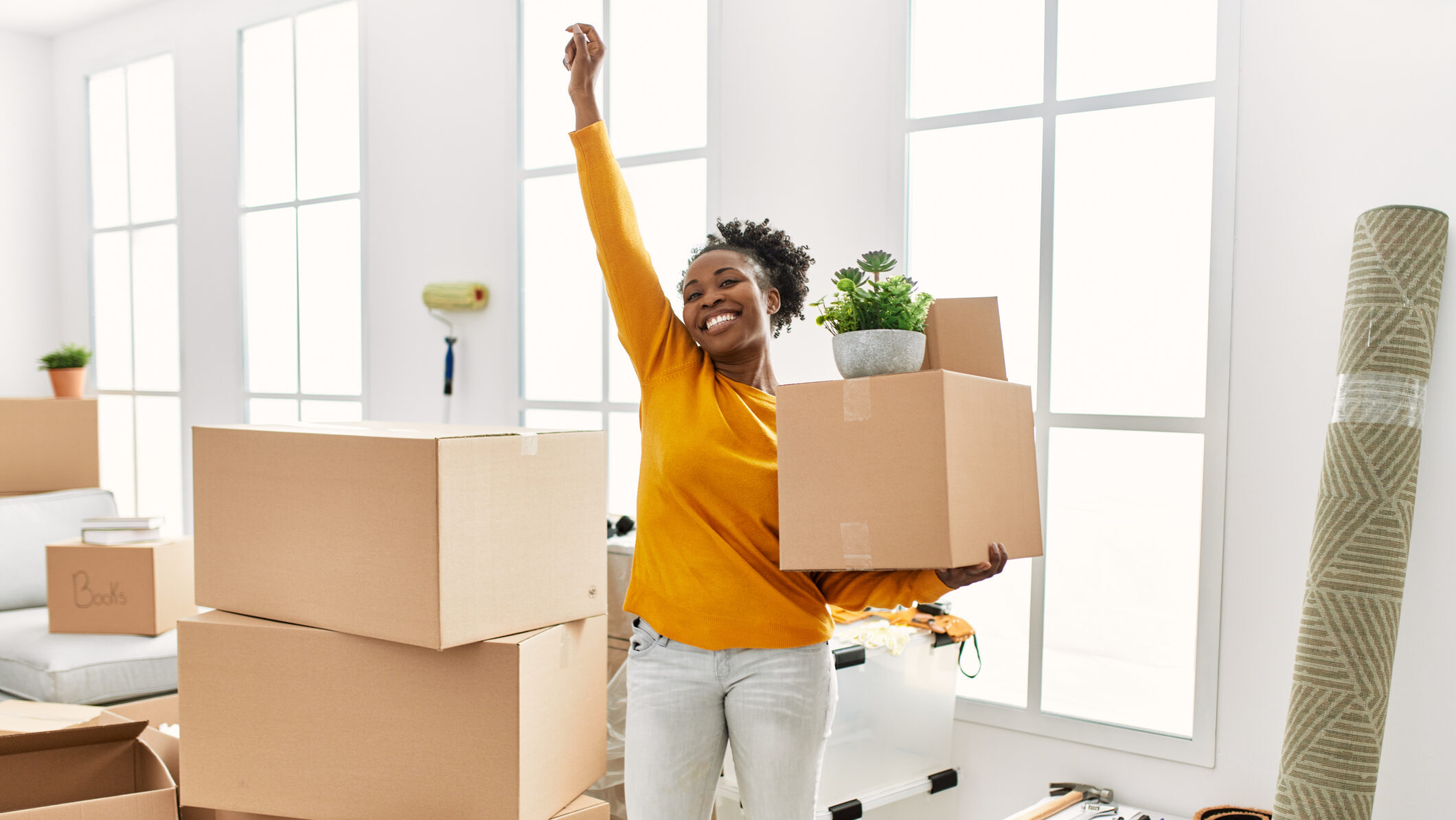 African american woman holding package standing with winner expression at new home